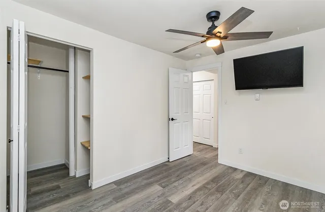 a view of an empty room with wooden floor and a ceiling fan