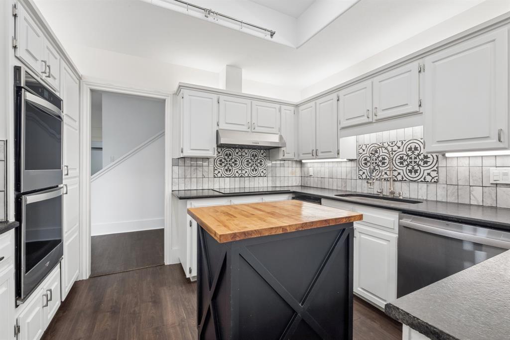 15539 Preston Road, Unit 1037 Dallas, TX 75248 - Photo 10 of 36 Kitchen featuring light gray cabinetry, dark countertops, black and white tile backsplash, stainless steel appliances, and a central island with a wood-finish top