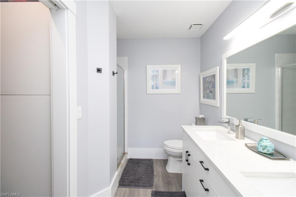 225 Robin Hood Circle, Unit 203 Naples, FL 34104 - Photo 39 of 50 Bathroom featuring dual bowl vanity, an enclosed shower, toilet, and wood-type flooring
