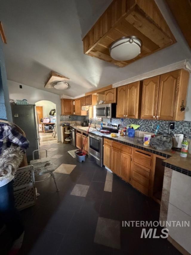 105 3rd Street Grand View, ID 83624 - Photo 11 of 19 Kitchen featuring wood-finish cabinetry, stainless steel appliances, mosaic tile backsplash, and a large arched doorway