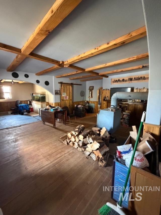 105 3rd Street Grand View, ID 83624 - Photo 12 of 19 Spacious room featuring exposed wood ceiling beams, wood-finish flooring, and a wood-burning stove with metal flue