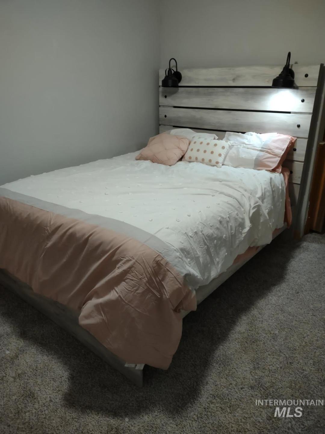 105 3rd Street Grand View, ID 83624 - Photo 18 of 19 Built-in wood-finish headboard with integrated sconce lighting, neutral wall paint, and gray carpet flooring