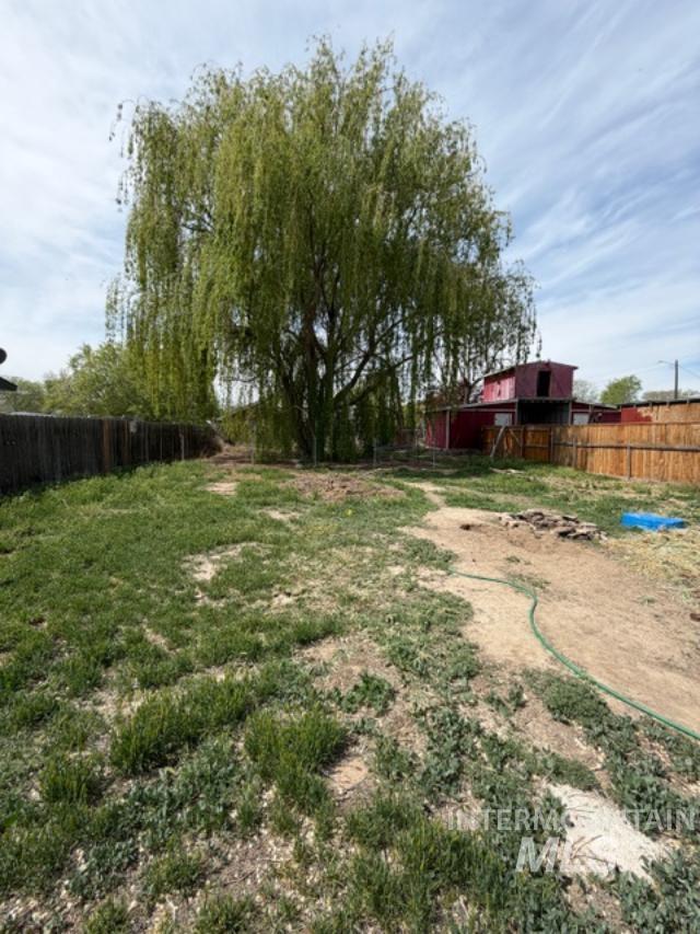 105 3rd Street Grand View, ID 83624 - Photo 8 of 19 Expansive backyard featuring a mature weeping willow tree, partial wood-panel fencing, and a red shed structure