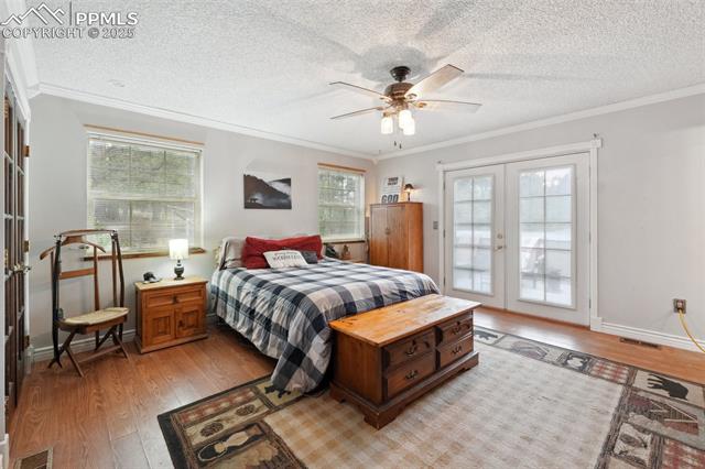 7475 Chirgiton Road Colorado Springs, CO 80908 - Photo 18 of 38 Bedroom with french doors, light wood finished floors, multiple windows, access to outside, and a textured ceiling