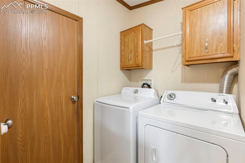 13335 Gymkhana Road Peyton, CO 80831 - Photo 24 of 38 Dedicated laundry space featuring a white top-load washer and dryer set, two overhead wood-finish cabinets with silver hardware, and a hanging rod