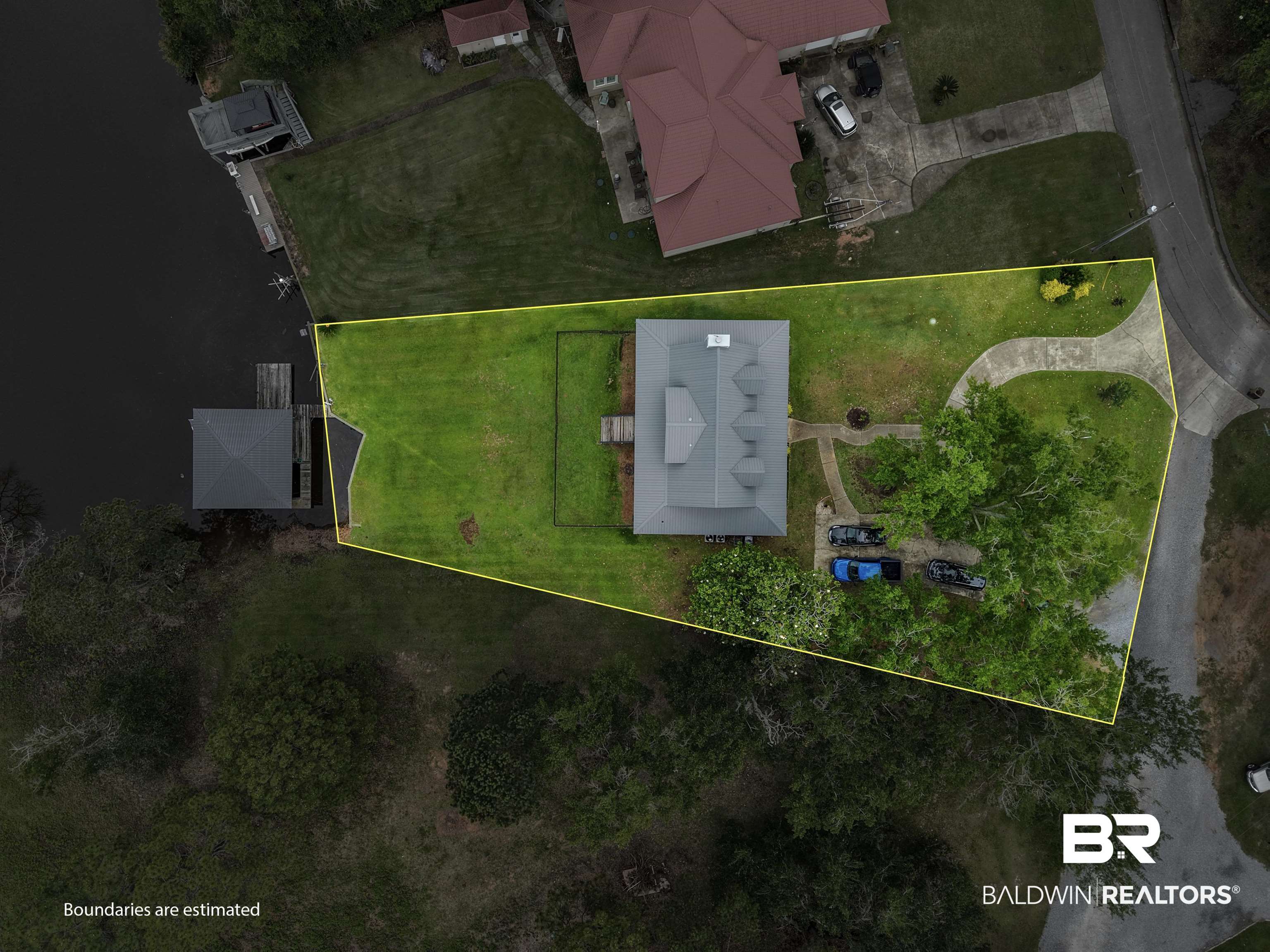 12171 Marguerite Drive Coden, AL 36523 - Photo 42 of 44 Waterfront property featuring a detached boathouse, private dock, expansive green lawn, and a curved driveway leading to the main residence
