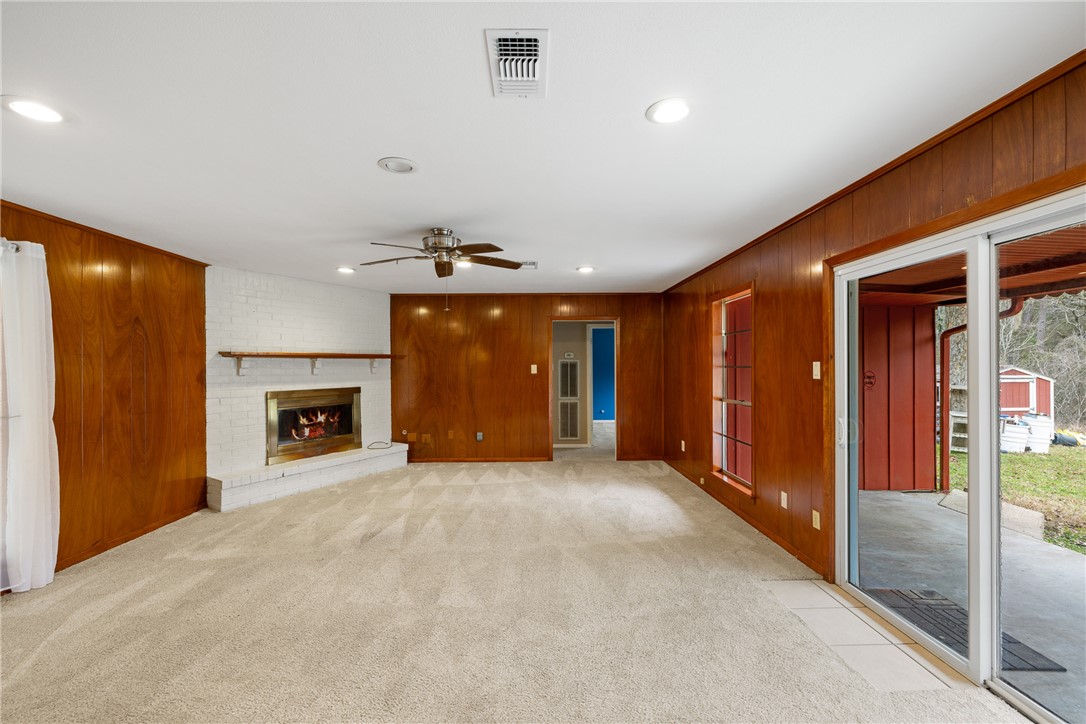 29 Dogwood Road Huntsville, TX 77320 - Photo 13 of 39 Unfurnished living room with wood walls, light colored carpet, a brick fireplace, a ceiling fan, and recessed lighting