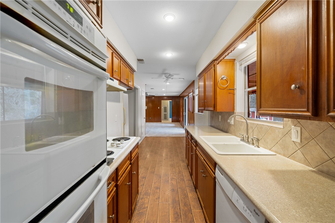 29 Dogwood Road Huntsville, TX 77320 - Photo 16 of 39 Kitchen with brown cabinets, white appliances, dark wood-style flooring, decorative backsplash, and a ceiling fan