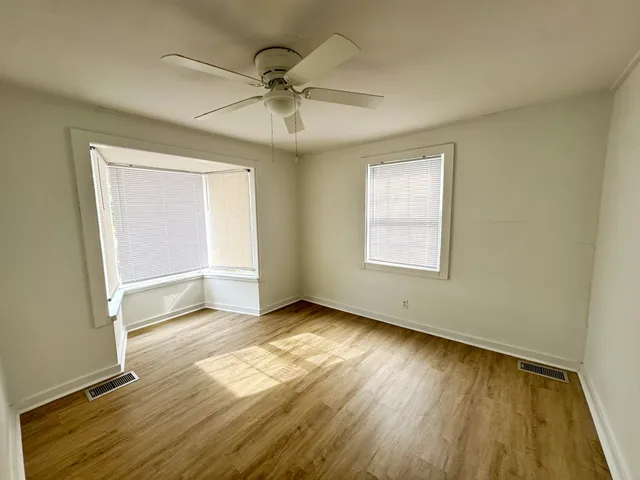 an empty room with wooden floor fan and windows