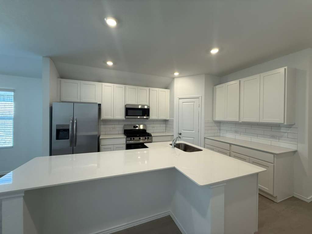 623 Sormonne Loop Kyle, TX 78640 - Photo 11 of 40 Kitchen featuring appliances with stainless steel finishes, white cabinets, decorative backsplash, light stone countertops, and an island with sink
