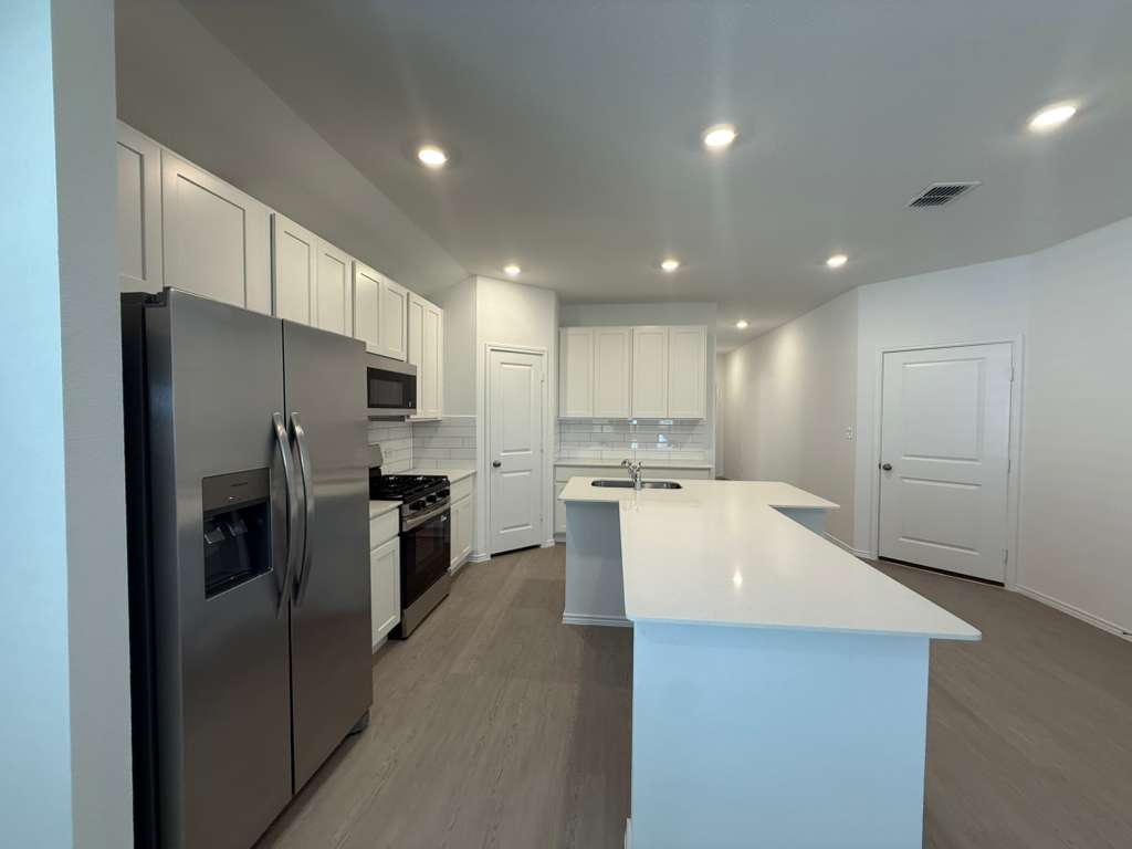 623 Sormonne Loop Kyle, TX 78640 - Photo 12 of 40 Kitchen with stainless steel appliances, dark wood-style flooring, backsplash, white cabinets, and an island with sink