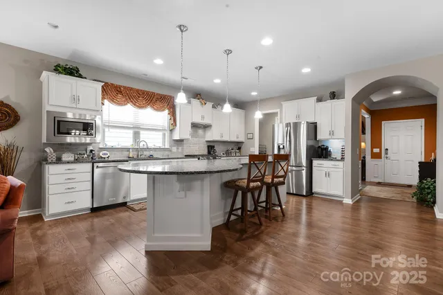 a kitchen with stainless steel appliances kitchen island granite countertop a stove a sink a refrigerator and white cabinets with wooden floor