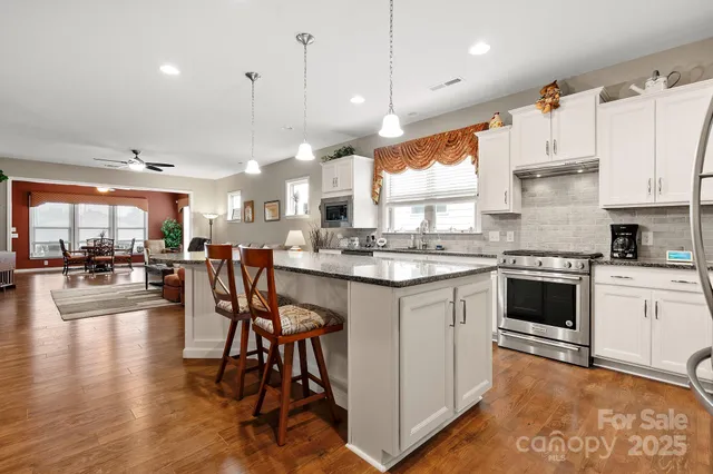 a kitchen with stainless steel appliances granite countertop a stove a sink a oven a dining table and chairs with wooden floor