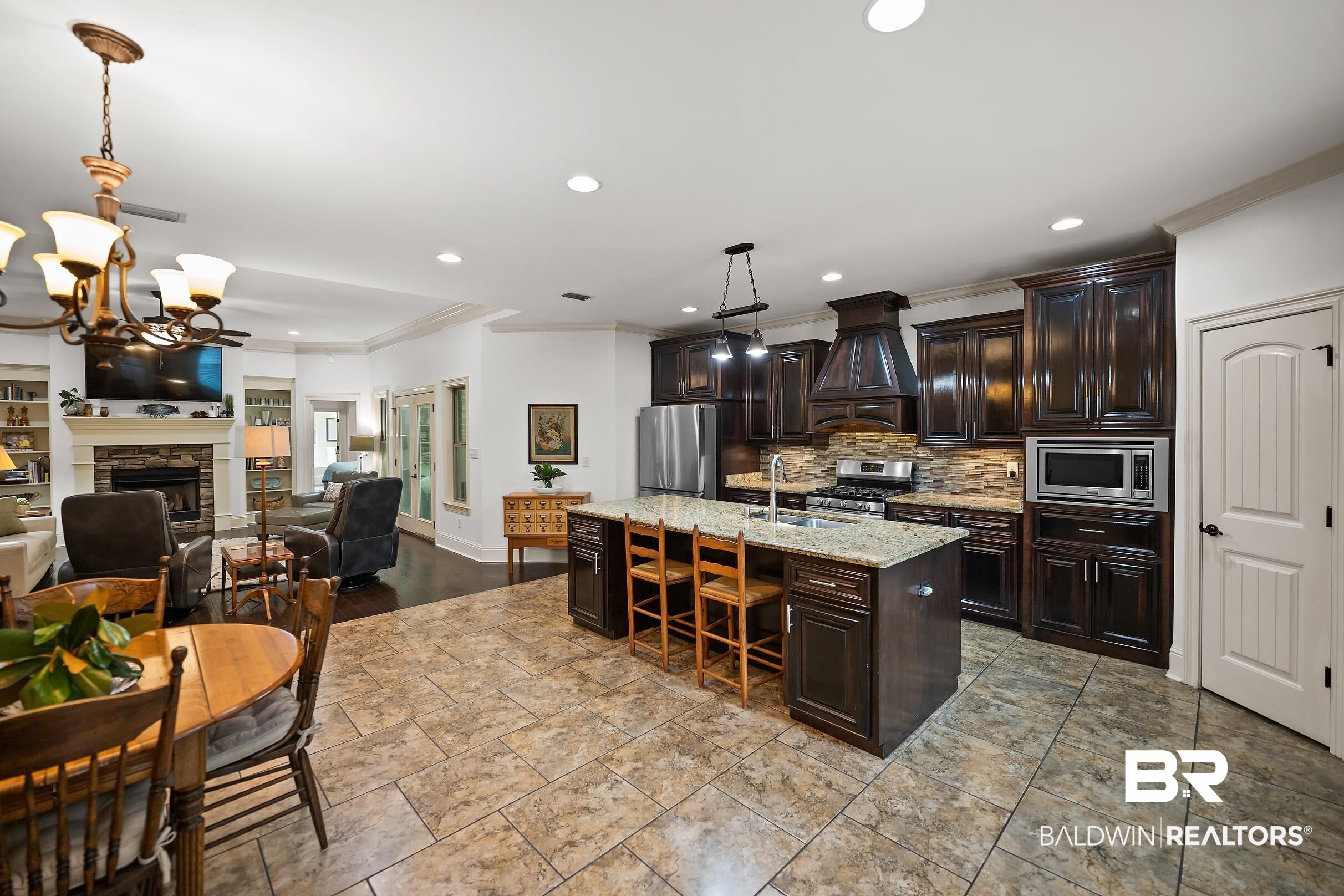313 Pecan Ridge Boulevard Fairhope, AL 36532 - Photo 28 of 51 Open-concept kitchen and living area featuring dark wood cabinetry, a central island with bar seating, and stone-finish flooring