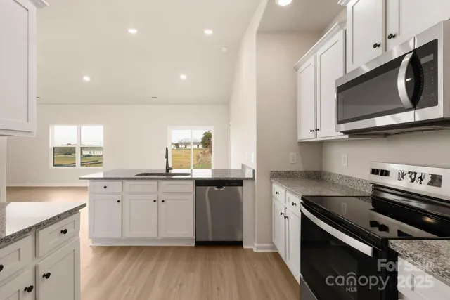 a kitchen with stainless steel appliances white cabinets granite counter tops a stove a sink and hard wood floors