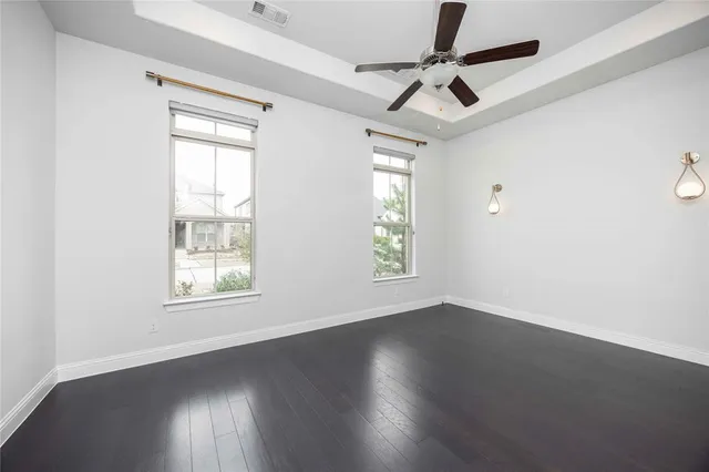 an empty room with wooden floor fan and windows