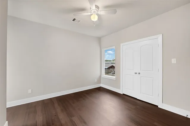 an empty room with wooden floor closet and windows