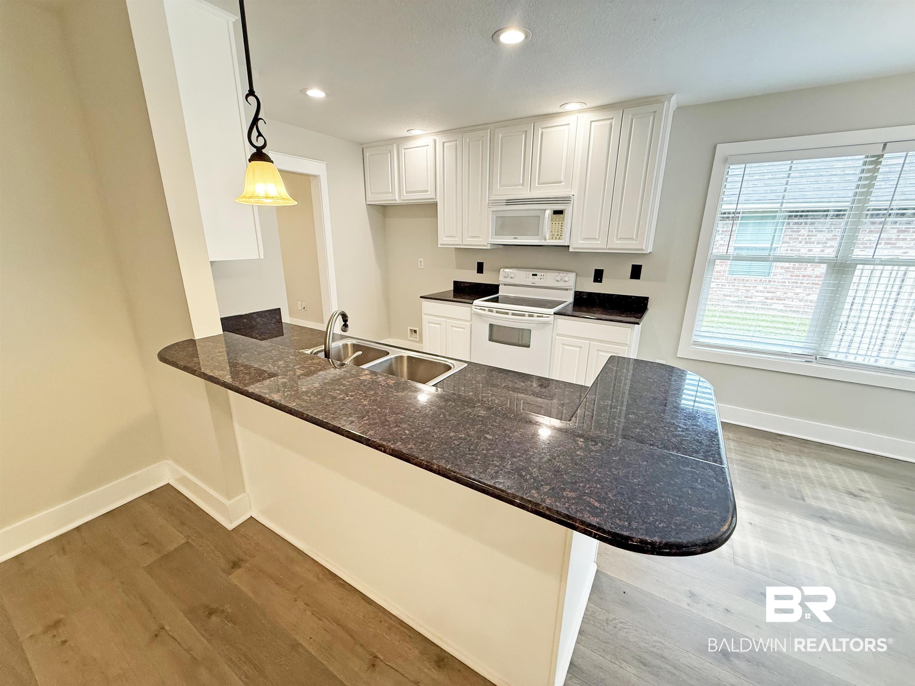 22023 Garland Loop Silverhill, AL 36576 - Photo 8 of 33 Kitchen featuring white appliances, wood finished floors, a peninsula, dark stone countertops, and white cabinets