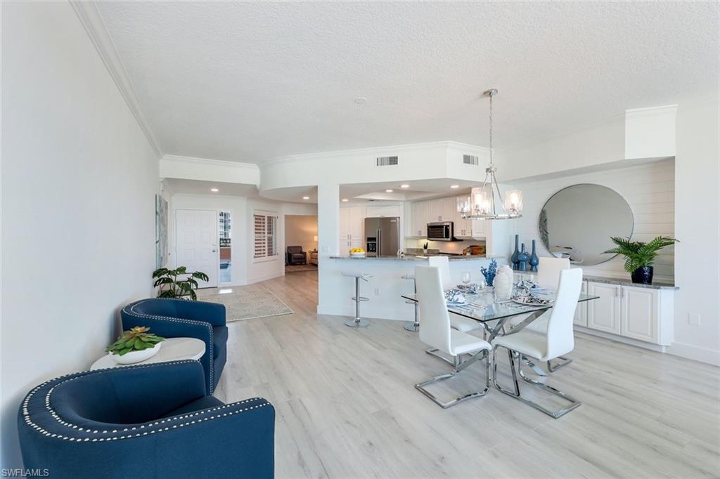 269 Barefoot Beach Boulevard, Unit 403 Bonita Springs, FL 34134 - Photo 9 of 27 Dining area featuring ornamental molding, a chandelier, light wood-type flooring, a textured ceiling, and baseboards