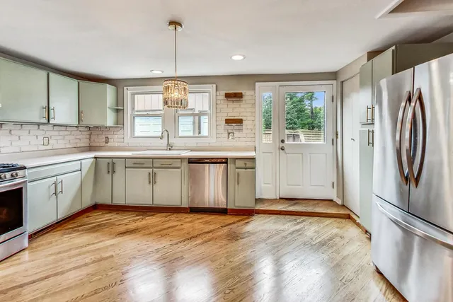 a kitchen with stainless steel appliances granite countertop a refrigerator a sink dishwasher a stove with white cabinets and wooden floor