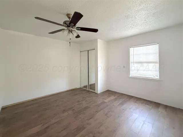 an empty room with wooden floor a ceiling fan and windows