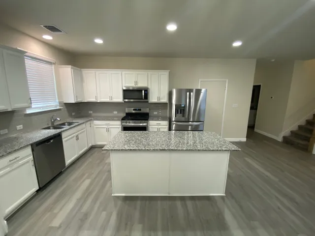 a large kitchen with stainless steel appliances granite countertop a stove a sink dishwasher a microwave oven and a refrigerator with wooden floor