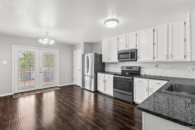 a kitchen with granite countertop a refrigerator a stove a sink cabinets and wooden floor