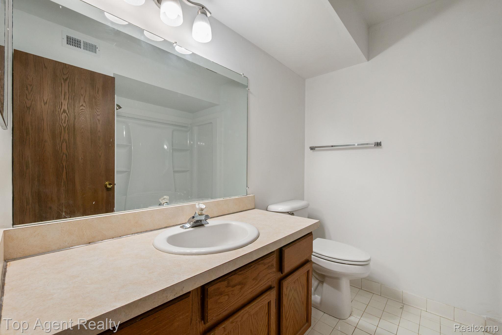 23420 Middlebelt Road Farmington, MI 48336 - Photo 15 of 32 Bathroom featuring a large vanity mirror, built-in vanity with wood-finish cabinetry, a single basin sink, and a toilet