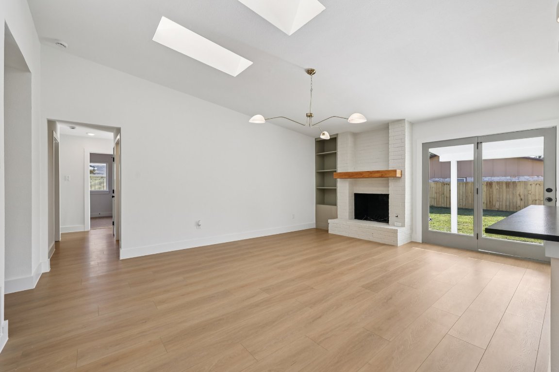 10424 Quail Ridge Drive Austin, TX 78758 - Photo 9 of 37 Unfurnished living room with a skylight, light wood-style flooring, built in shelves, a fireplace, and vaulted ceiling
