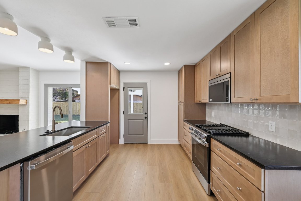 10424 Quail Ridge Drive Austin, TX 78758 - Photo 12 of 37 Kitchen with stainless steel appliances, dark stone countertops, light wood-style flooring, backsplash, and recessed lighting