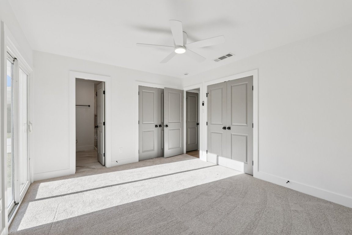 10424 Quail Ridge Drive Austin, TX 78758 - Photo 16 of 37 Unfurnished bedroom with two closets, carpet flooring, ceiling fan, and ensuite bath