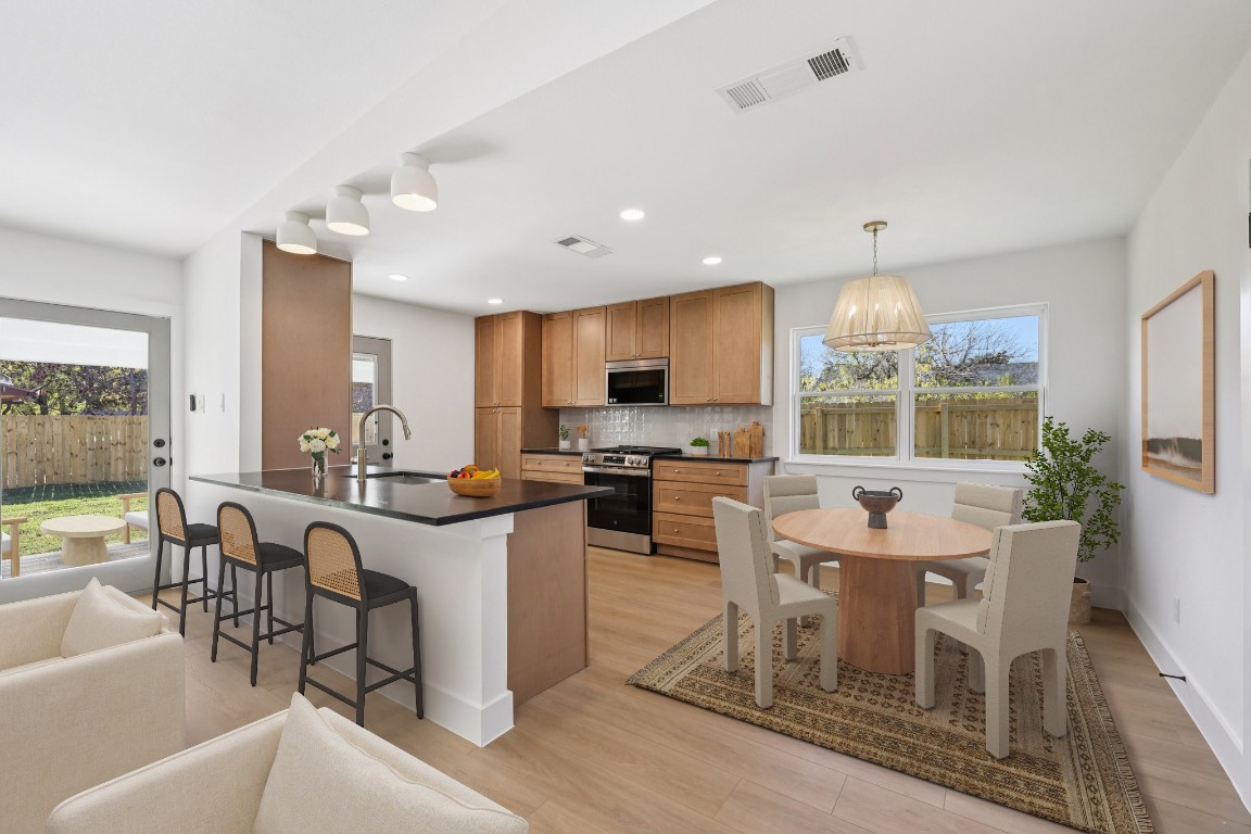 10424 Quail Ridge Drive Austin, TX 78758 - Photo 3 of 37 Kitchen featuring dark countertops, a kitchen breakfast bar, brown cabinets, appliances with stainless steel finishes, and backsplash