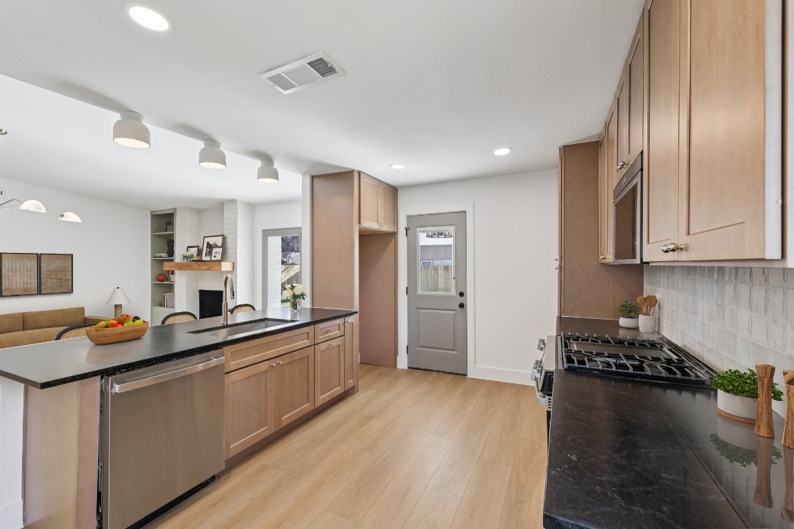 10424 Quail Ridge Drive Austin, TX 78758 - Photo 34 of 37 Kitchen with appliances with stainless steel finishes, open floor plan, light wood-type flooring, dark stone countertops, and recessed lighting