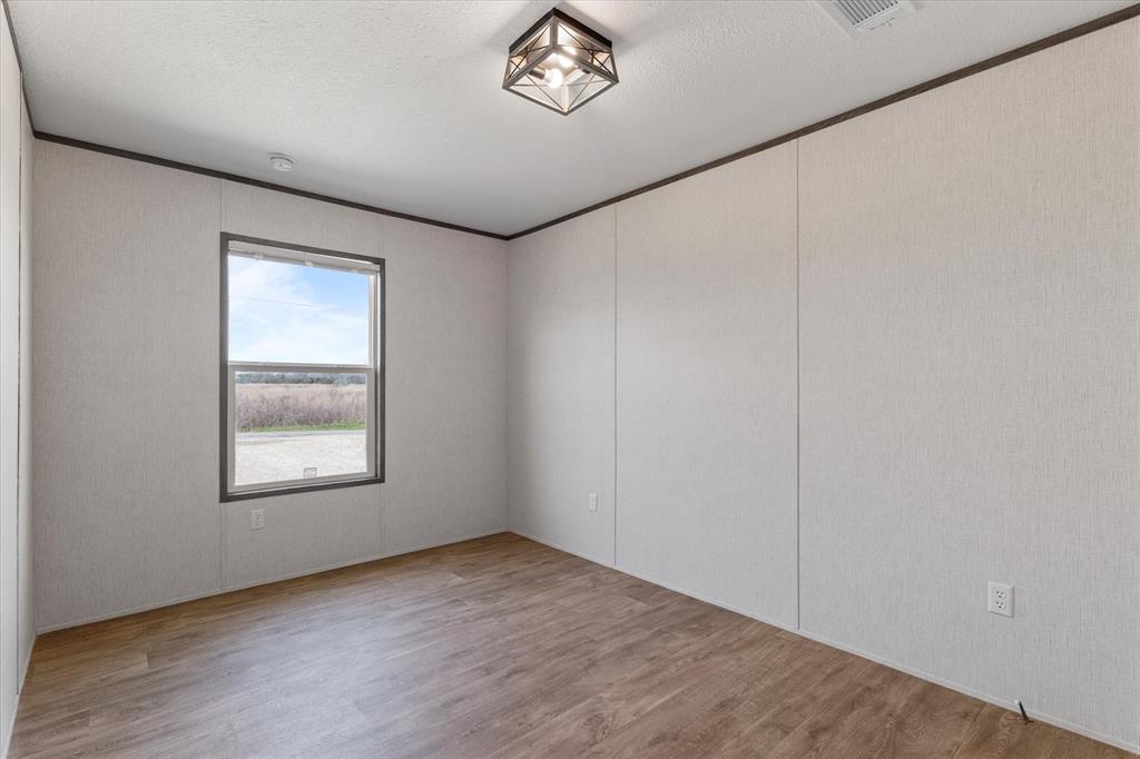 3888 Sandusky Road Whitesboro, TX 76273 - Photo 25 of 39 Unfurnished room featuring visible vents, a textured ceiling, wood finished floors, and crown molding