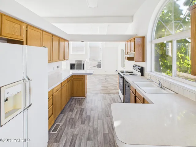 a living room with stainless steel appliances granite countertop a refrigerator a sink dishwasher a stove and white countertops with wooden floor