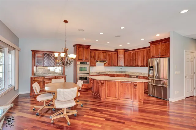 a kitchen with stainless steel appliances granite countertop a stove top oven a dining table and chairs with wooden floor