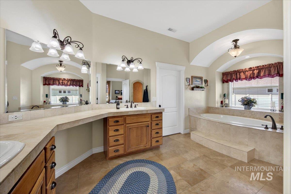 414 East Shafer View Drive Meridian, ID 83642 - Photo 21 of 50 Primary Bath featuring Tiled flooring, a built-in soaking tub with tiled surround, Walk-In tiled shower, a double vanity with wood cabinetry, a large mirror, private commode room