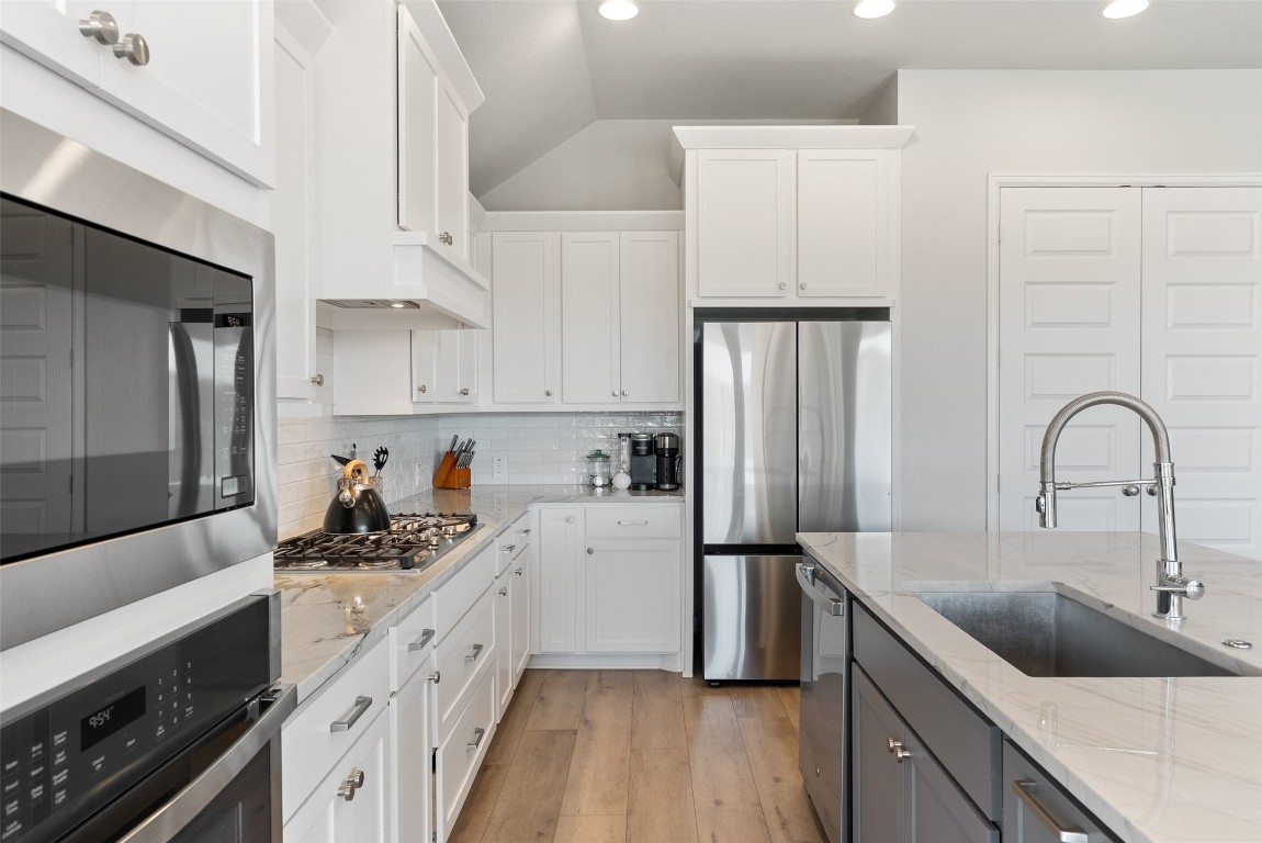 321 Allegheny Way Kyle, TX 78640 - Photo 16 of 40 Kitchen with stainless steel appliances, white cabinets, light stone counters, vaulted ceiling, and recessed lighting