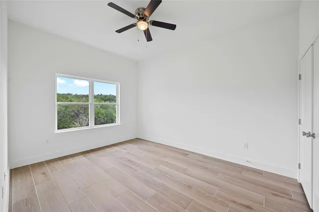 an empty room with wooden floor fan and windows