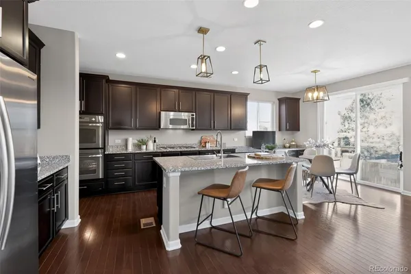 a kitchen with stainless steel appliances granite countertop a stove top oven a sink a dining table and chairs with wooden floor