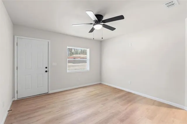 an empty room with wooden floor fan and windows