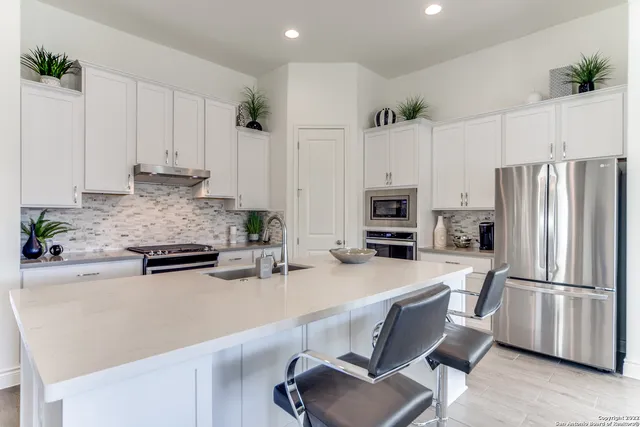 a kitchen with stainless steel appliances a stove a sink a refrigerator and white cabinets