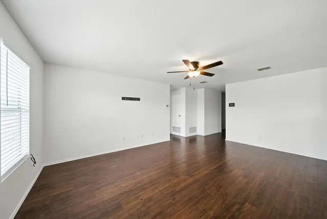 an empty room with wooden floor chandelier fan and windows