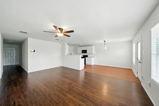 a view of an empty room with wooden floor and a ceiling fan