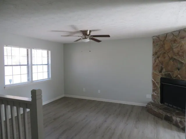 an empty room with wooden floor fan and windows