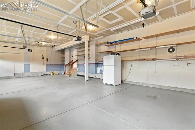 Garage featuring a garage door opener and white fridge