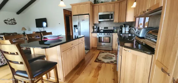 a kitchen with stainless steel appliances kitchen island granite countertop a stove top oven a sink a dining table and chairs with wooden floor