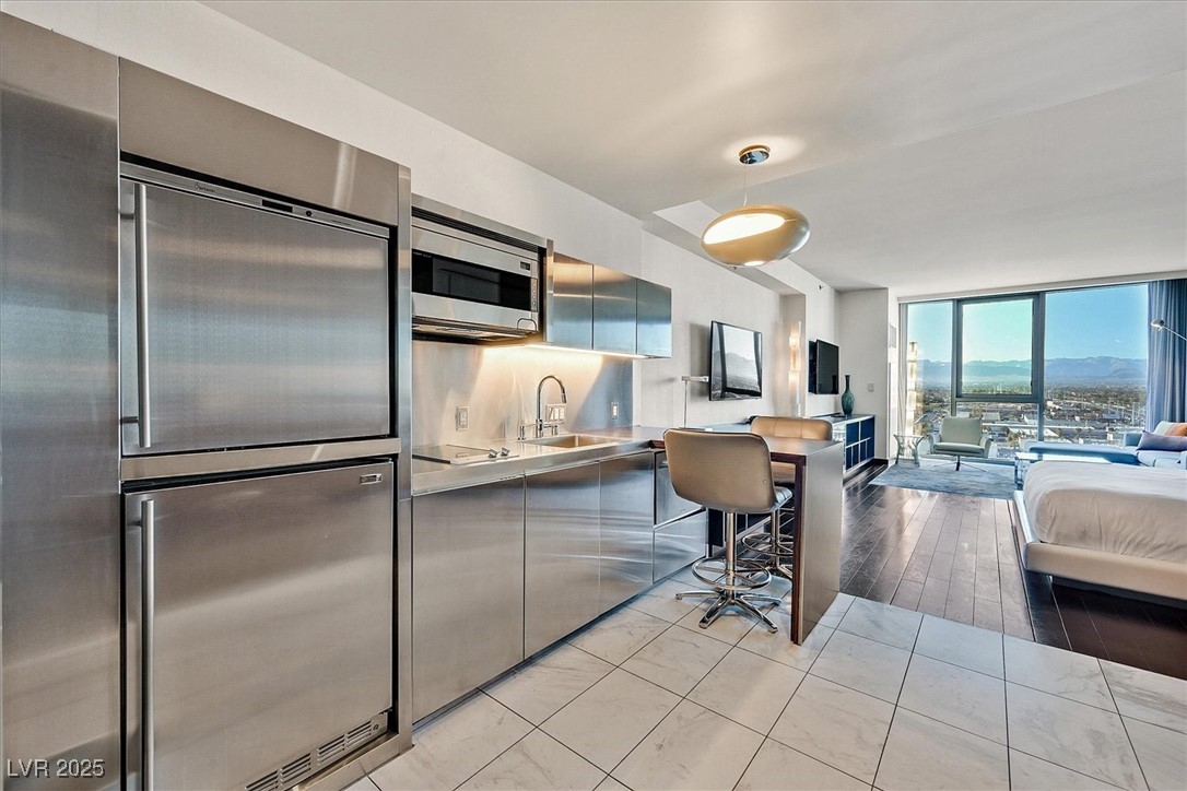 Kitchen with a wall of windows, modern cabinets, a sink, stainless steel countertops, and built in appliances