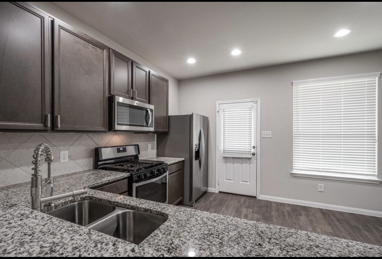 17542 Holroyd Road Humble, TX 77346 - Photo 6 of 16 a kitchen with stainless steel appliances granite countertop a sink a stove and a refrigerator with wooden floor