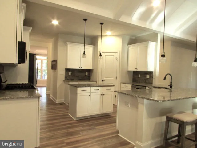 a kitchen with stainless steel appliances granite countertop a sink a stove a refrigerator and white cabinets with wooden floor